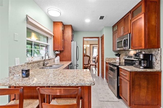 kitchen featuring visible vents, a peninsula, a sink, decorative backsplash, and appliances with stainless steel finishes