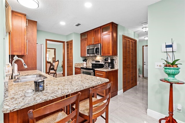 kitchen featuring a breakfast bar area, decorative backsplash, brown cabinets, appliances with stainless steel finishes, and a sink