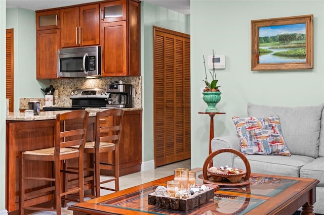 kitchen featuring glass insert cabinets, appliances with stainless steel finishes, a breakfast bar area, decorative backsplash, and light stone countertops