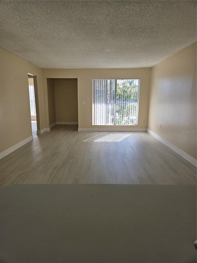 unfurnished room featuring baseboards, a textured ceiling, and wood finished floors