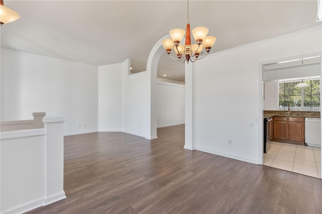 unfurnished dining area featuring baseboards, arched walkways, an inviting chandelier, and wood finished floors