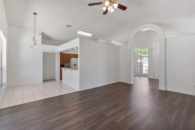 unfurnished living room featuring a ceiling fan, visible vents, light wood-style flooring, arched walkways, and vaulted ceiling