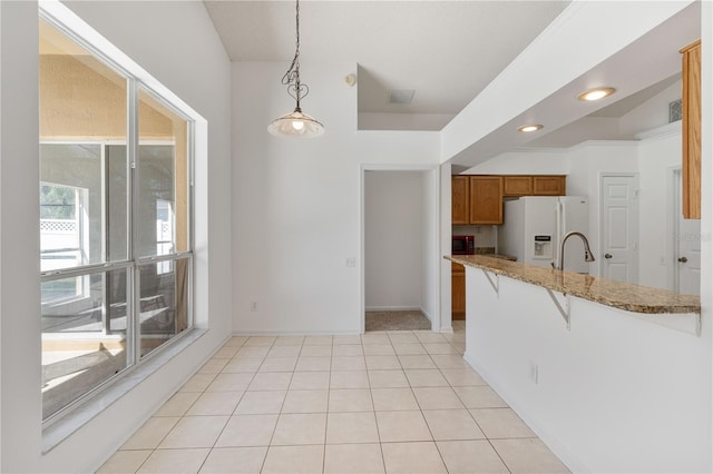 kitchen featuring white fridge with ice dispenser, a breakfast bar, hanging light fixtures, light tile patterned flooring, and brown cabinetry