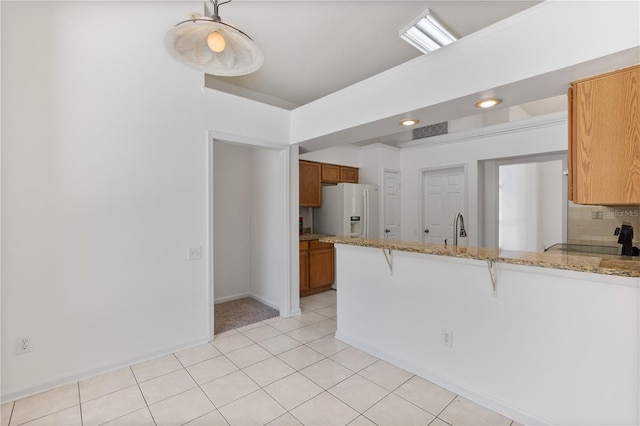 kitchen with brown cabinets, a peninsula, white refrigerator with ice dispenser, a kitchen bar, and tasteful backsplash