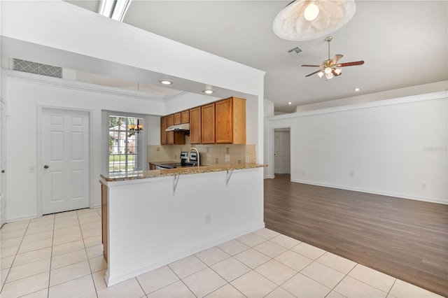 kitchen featuring electric range, light tile patterned floors, visible vents, and brown cabinets