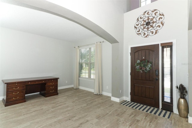 entrance foyer with light wood-style floors, arched walkways, a towering ceiling, and baseboards