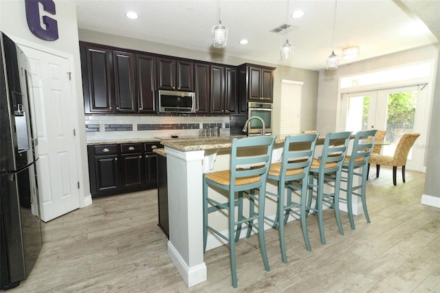 kitchen with visible vents, light wood-style flooring, stainless steel microwave, fridge with ice dispenser, and tasteful backsplash