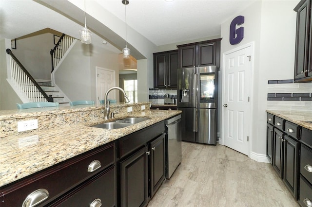 kitchen with hanging light fixtures, light wood-style flooring, arched walkways, stainless steel appliances, and a sink