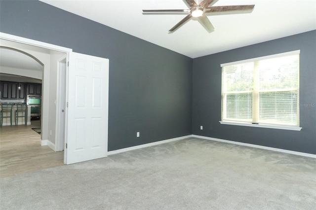 spare room with arched walkways, light colored carpet, baseboards, and a ceiling fan