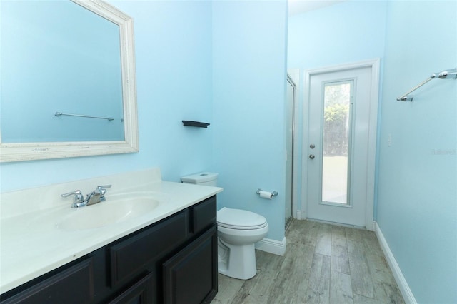 bathroom featuring toilet, wood finished floors, a shower stall, baseboards, and vanity