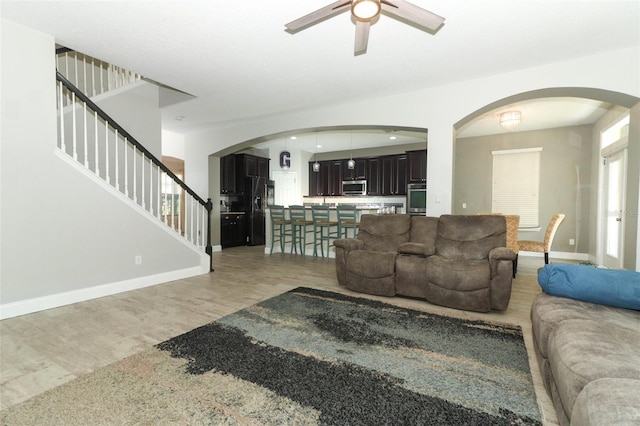 living room featuring baseboards, light wood-style floors, arched walkways, and ceiling fan