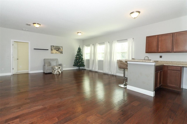 kitchen featuring a breakfast bar, dark wood-style floors, open floor plan, a peninsula, and baseboards