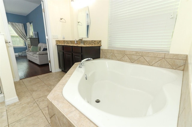 bathroom featuring tile patterned floors, ensuite bath, baseboards, a bath, and vanity