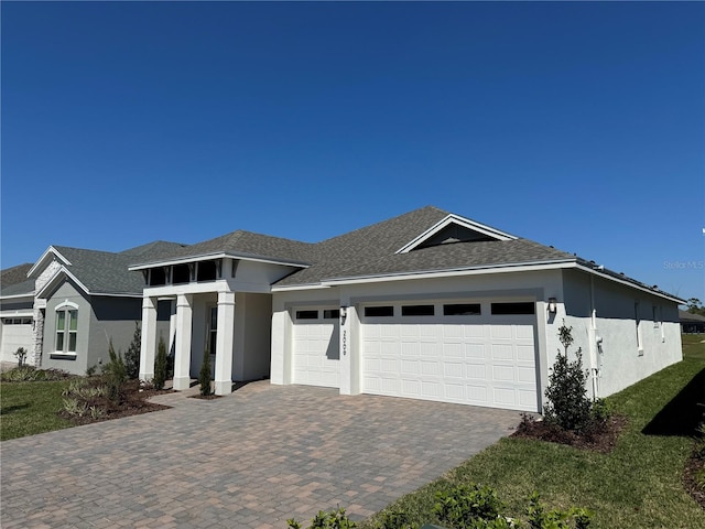 view of front of house with a shingled roof, decorative driveway, a garage, and stucco siding