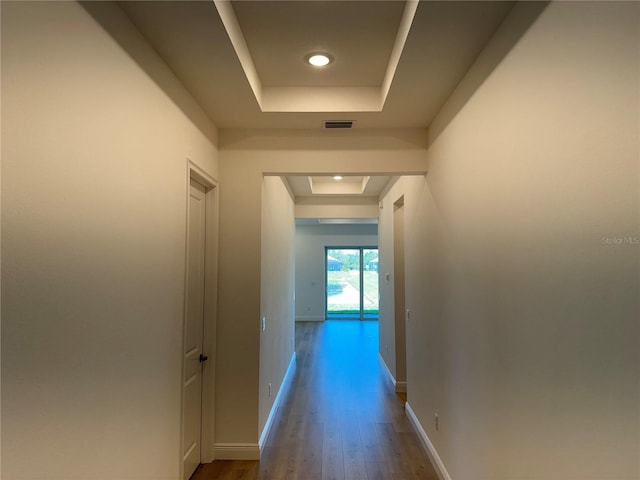 hall featuring a raised ceiling, visible vents, baseboards, and dark wood-type flooring