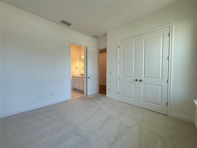 unfurnished bedroom with visible vents, ensuite bathroom, a closet, baseboards, and light colored carpet