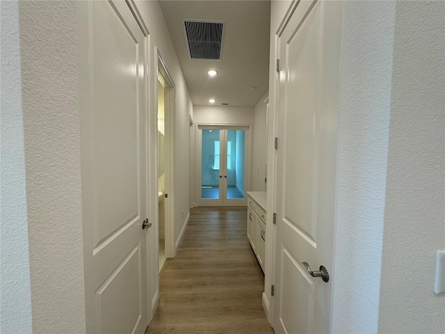 hall with wood finished floors, visible vents, a textured wall, and baseboards