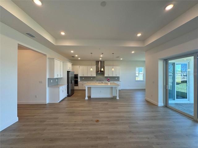 kitchen featuring wall chimney range hood, open floor plan, appliances with stainless steel finishes, and a sink