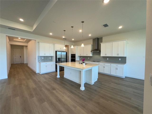 kitchen with visible vents, a sink, white cabinetry, stainless steel appliances, and wall chimney exhaust hood