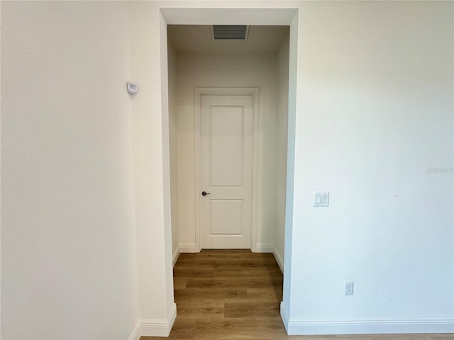 hallway featuring visible vents, baseboards, and wood finished floors