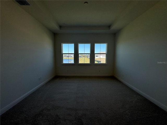 unfurnished room featuring visible vents, dark carpet, baseboards, and a tray ceiling