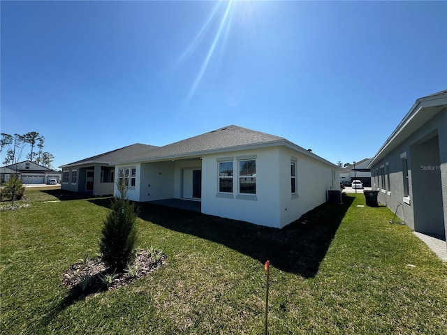 back of property with a shingled roof, a lawn, central AC, and stucco siding