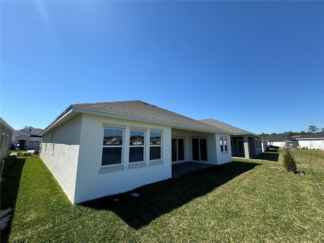 back of house featuring stucco siding, a lawn, and roof with shingles