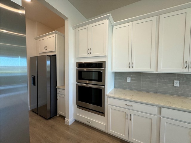 kitchen with wood finished floors, stainless steel appliances, white cabinets, decorative backsplash, and light stone countertops