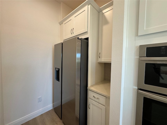 kitchen featuring baseboards, decorative backsplash, light wood-style flooring, stainless steel appliances, and white cabinetry