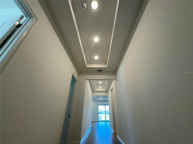 hallway with visible vents, baseboards, recessed lighting, wood finished floors, and a raised ceiling