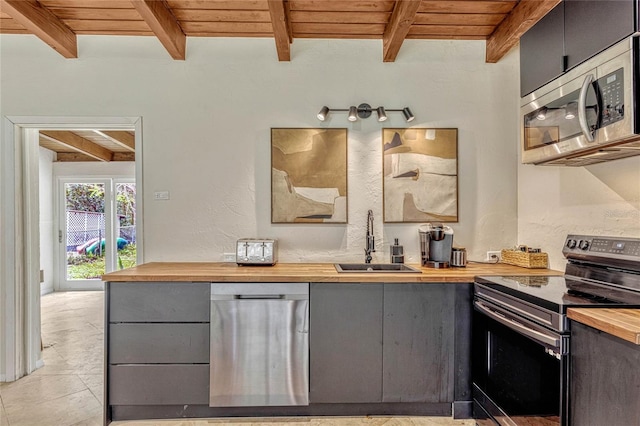 kitchen with gray cabinetry, stainless steel appliances, wood counters, and a sink