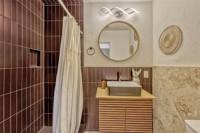 full bath featuring tiled shower, tile walls, vanity, and a textured wall