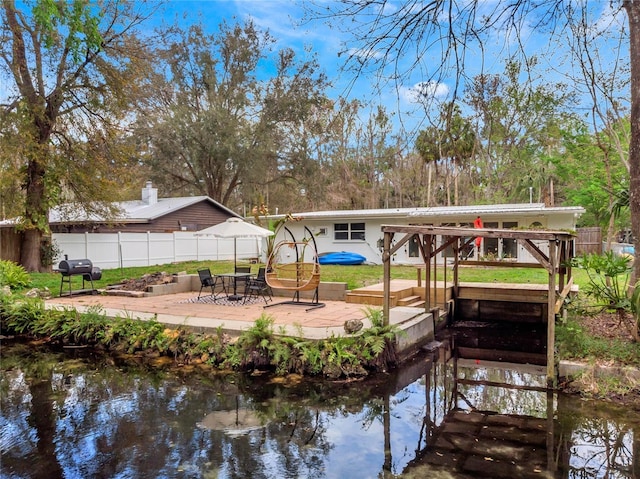 view of dock with a patio area, a water view, and fence