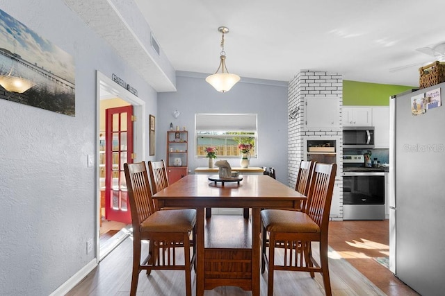 dining space featuring light wood-style floors, visible vents, and a textured wall