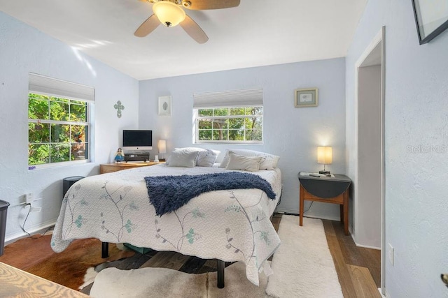 bedroom with a ceiling fan, multiple windows, wood finished floors, and baseboards