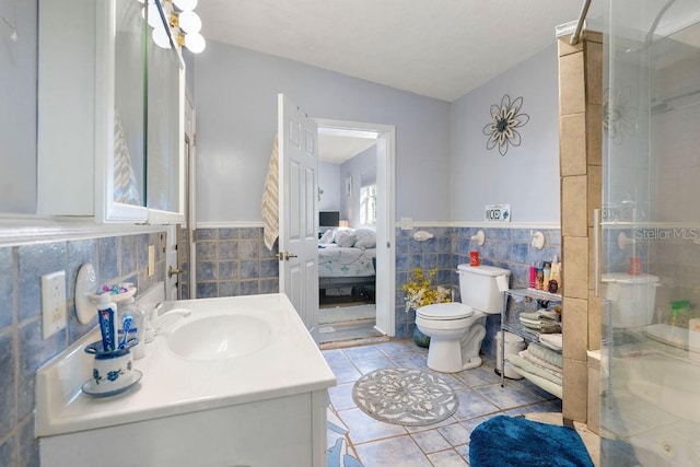 ensuite bathroom featuring a shower stall, a wainscoted wall, toilet, vanity, and tile walls