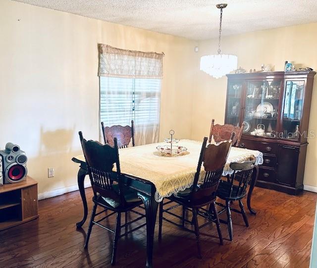 dining space featuring baseboards, a textured ceiling, an inviting chandelier, and dark wood-style flooring