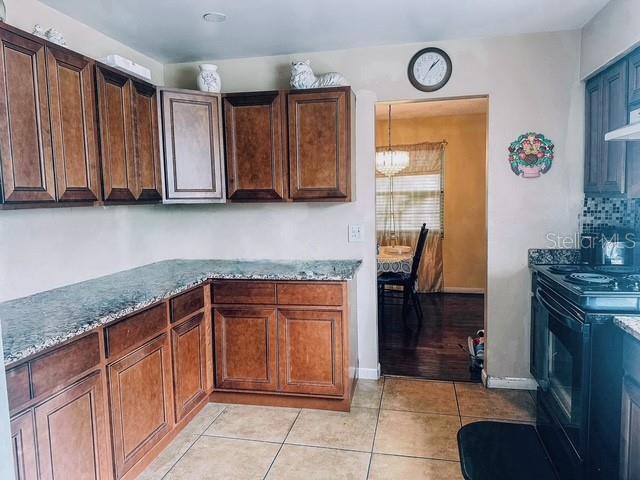 kitchen featuring light tile patterned floors, light stone countertops, baseboards, an inviting chandelier, and black range with electric stovetop