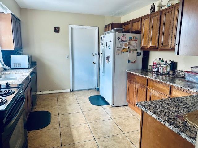 kitchen with light tile patterned floors, dark stone counters, and white appliances