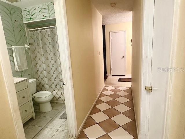 bathroom featuring wallpapered walls, baseboards, toilet, vanity, and a textured ceiling