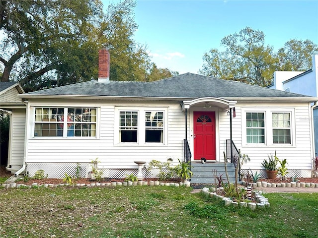 view of front of property featuring a chimney, a front yard, and a shingled roof