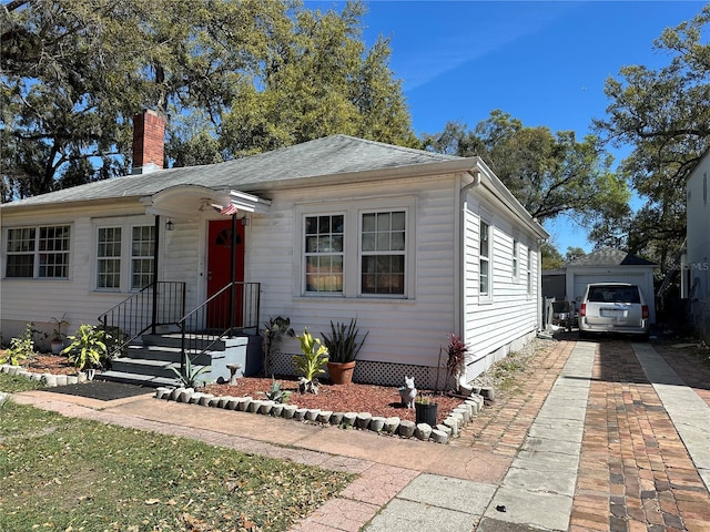 view of front facade with a garage, driveway, a chimney, and an outdoor structure