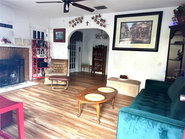 living area featuring visible vents, a fireplace, wood finished floors, arched walkways, and a ceiling fan