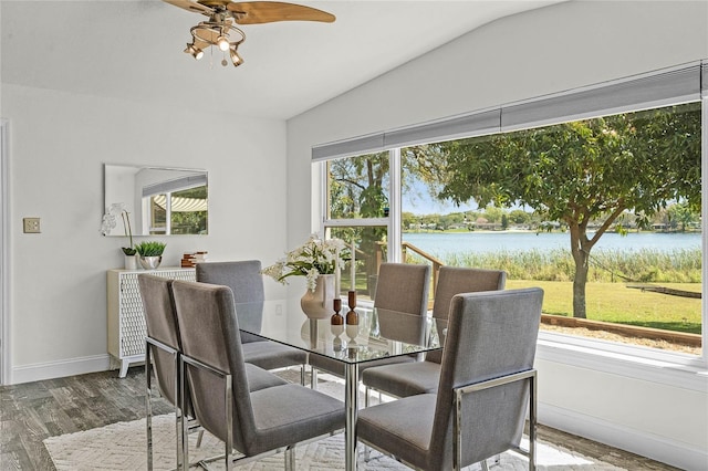 dining space with a water view, wood finished floors, baseboards, ceiling fan, and vaulted ceiling