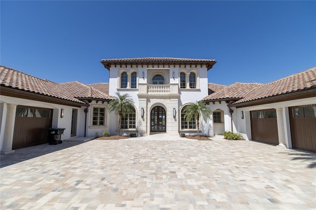 view of front of property featuring a balcony, stucco siding, a garage, a tiled roof, and decorative driveway