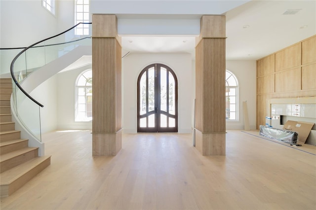 foyer entrance featuring a healthy amount of sunlight, decorative columns, stairs, french doors, and light wood-type flooring