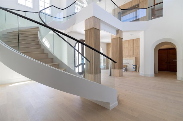 stairway with arched walkways, a towering ceiling, and wood finished floors