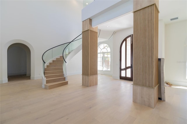 entrance foyer with visible vents, a high ceiling, light wood-style flooring, arched walkways, and stairs