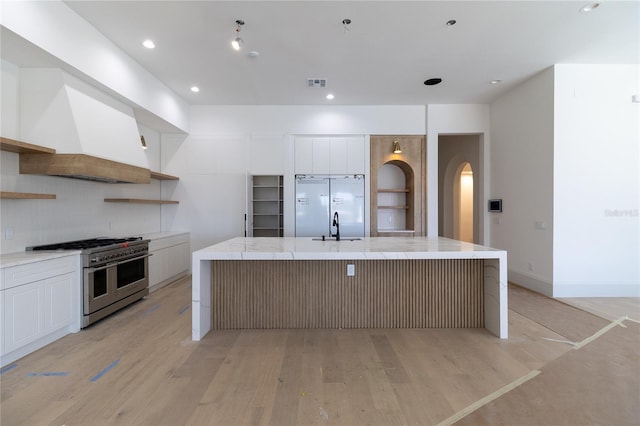 kitchen featuring visible vents, open shelves, built in fridge, light wood-style floors, and range with two ovens