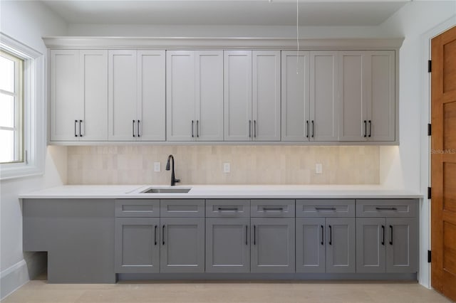 kitchen featuring backsplash, gray cabinetry, light countertops, and a sink